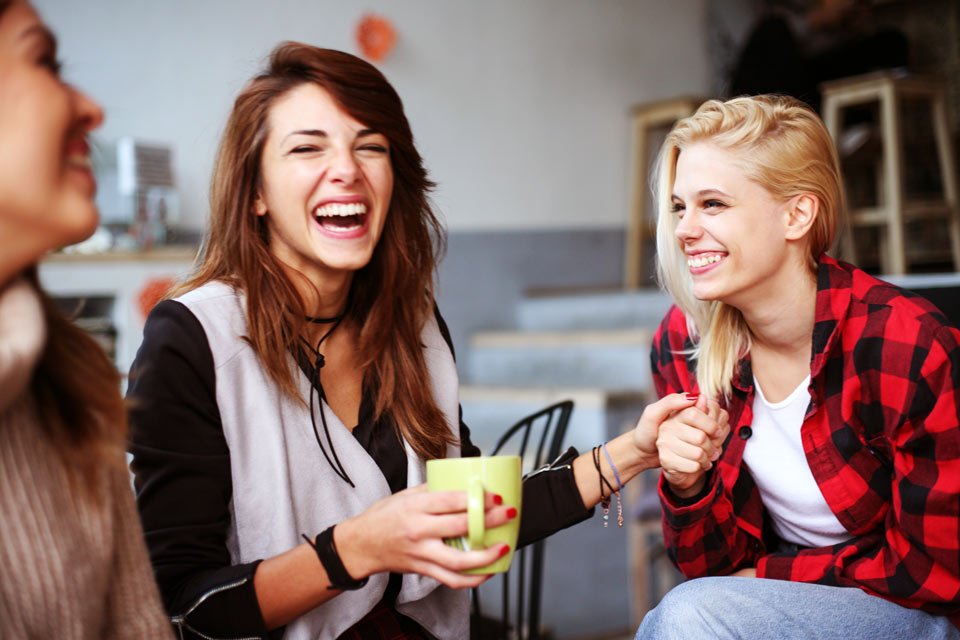 3 young adult women laughing in a coffee shop