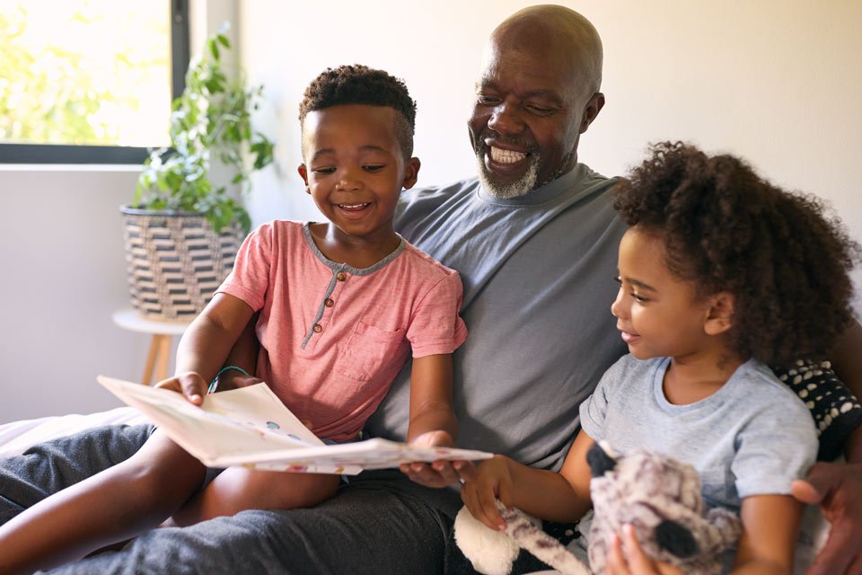 young dad with 2 kids reading a book together smiling