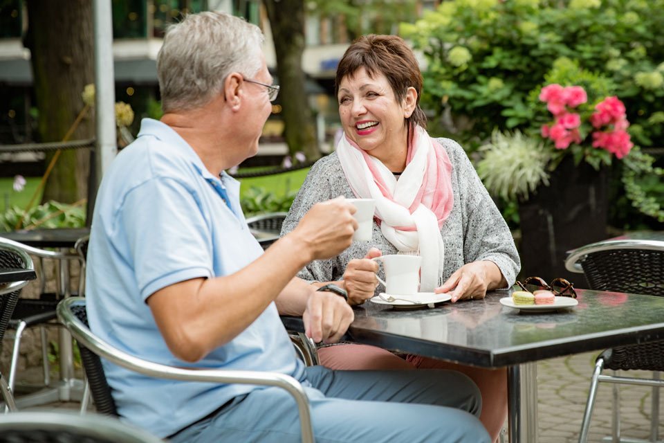 older man and woman laughing over a cup of coffee outside