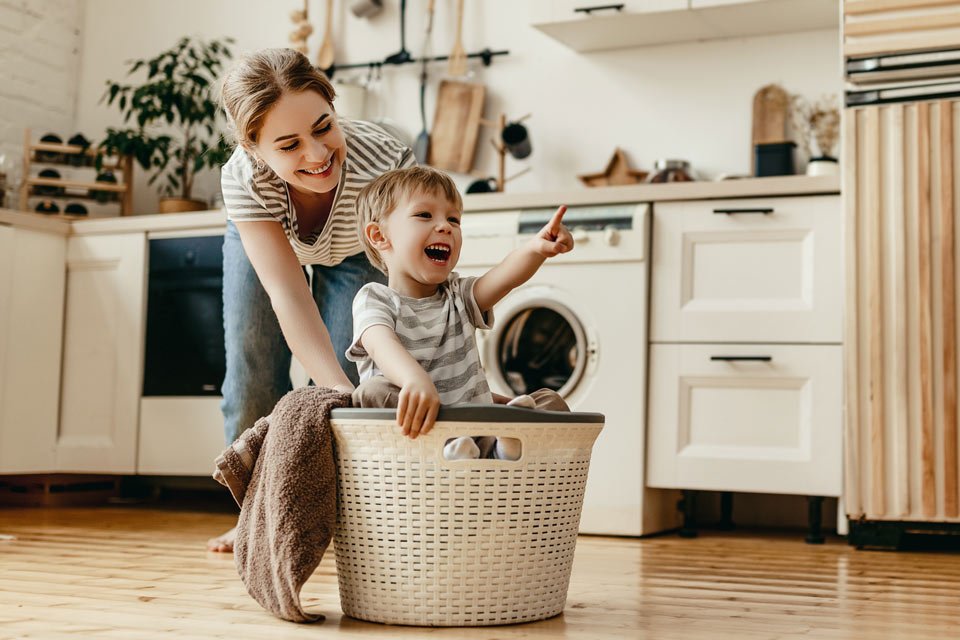 A mom pushing child around in a laundry basket, smiling