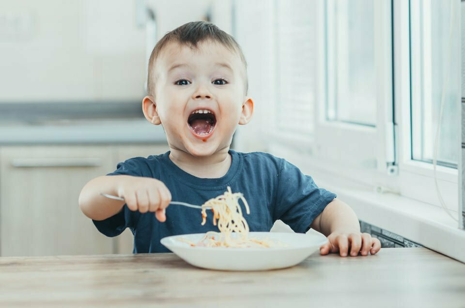 small child laughing while eating spaghetti